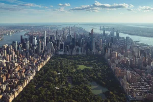 Birds eye view of central park and New York City skyline on a day with blue skies but some clouds.