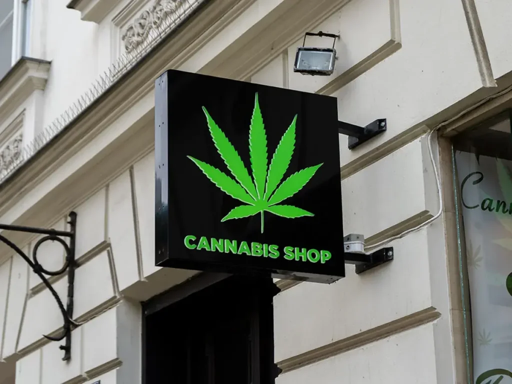 Bright green cannabis leaf on a black sign above a store labeled “Cannabis Shop” mounted on a classic urban building façade.