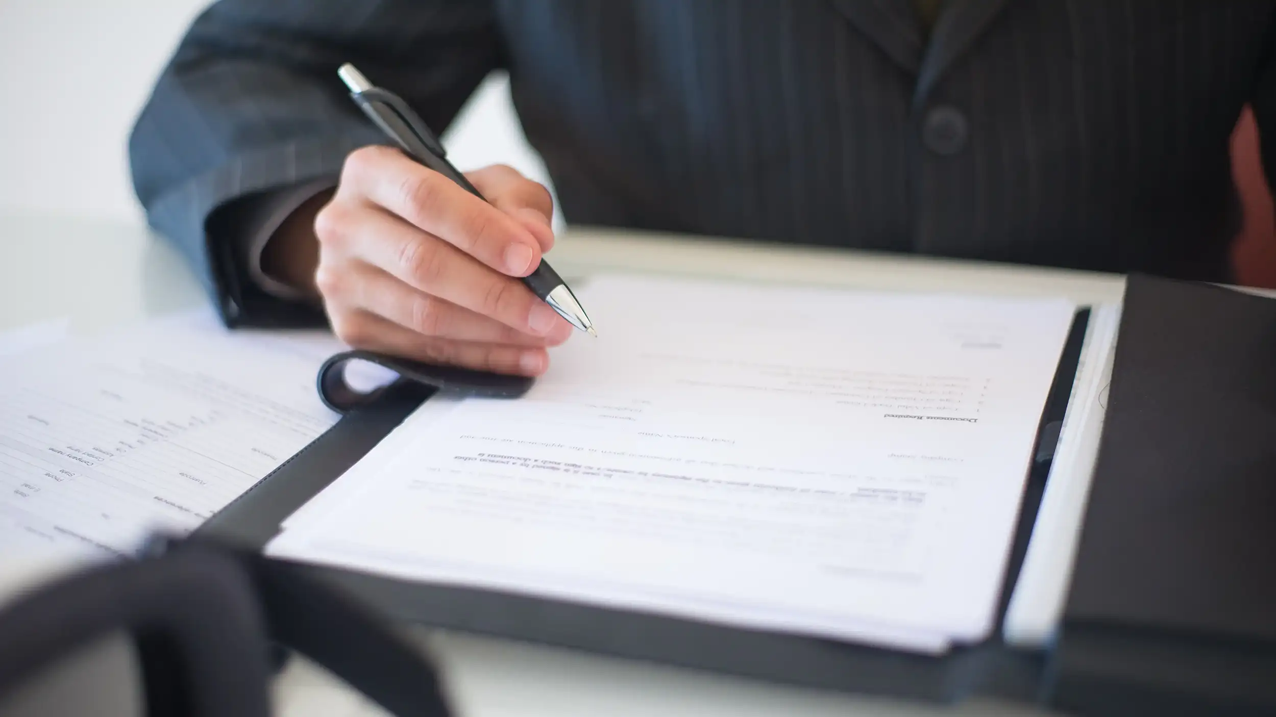 man in black suit writing in a document with a black pen