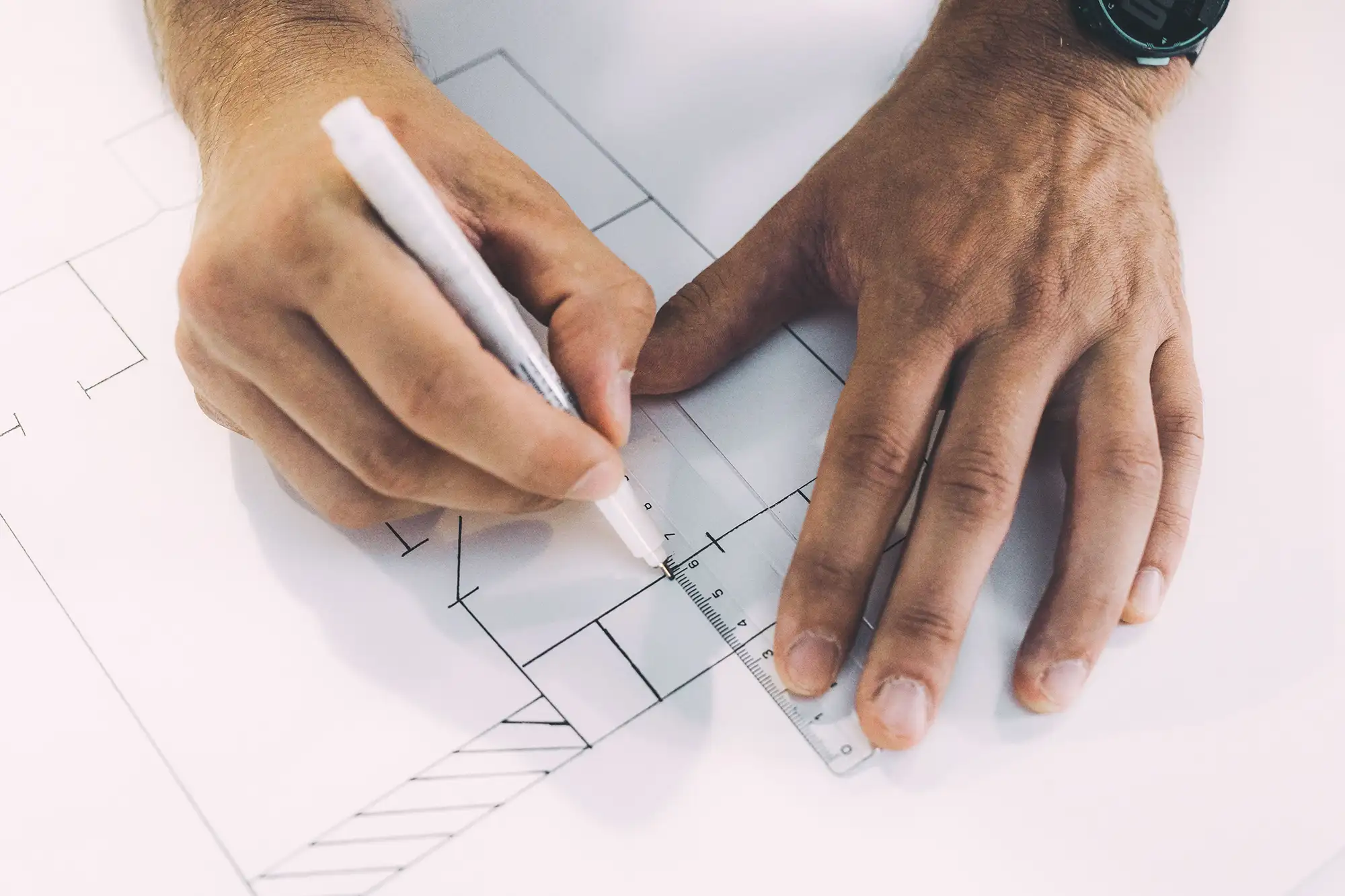 Hands using a ruler and pen to draft a compliant retail dispensary floor plan layout on architectural blueprints.