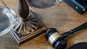 Bronze scales of justice resting next to a wooden gavel and a legal binder on a wooden desk.